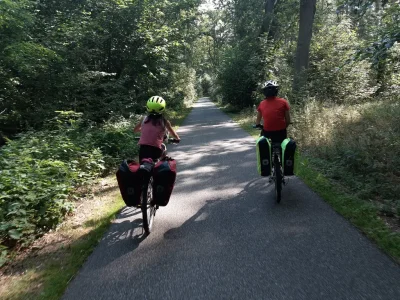 Deux enfants pédalent sur une voie verte en forêt, avec des sacoches sur leurs vélos