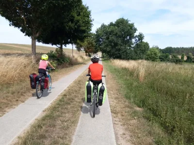 Deux enfants pédalent sur une voie agricole, avec des sacoches sur leurs vélos