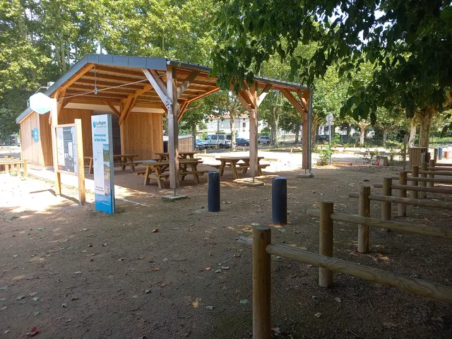 Zone d'accueil pour les cyclistes avec un abri en bois pour des tables de pique-nique, des barrières pour accrocher les vélos et des panneaux informatifs.